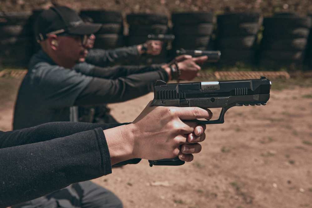 Primer plano de manos sosteniendo una pistola Córdova en un polígono de tiro con personas al fondo.